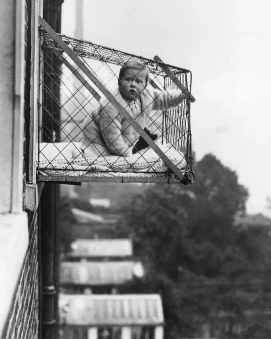Parenting in the 1930s: A baby hanging outside a window in a 'baby cage' designed to give infants fresh air and sunlight in crowded apartments