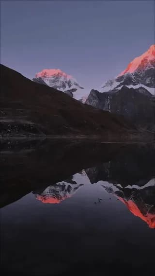 Sunrise alpenglow hitting the peaks of Huayhuash, Peru, reflected on a calm mountain lake