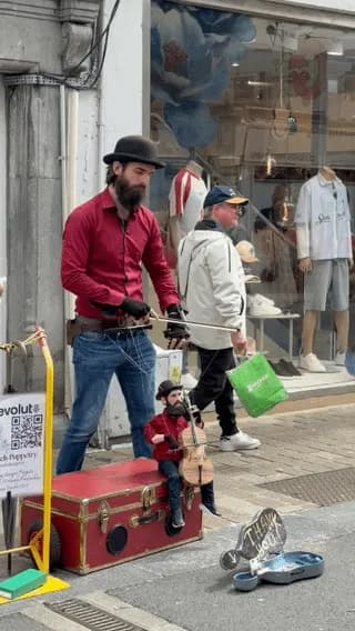 A street performer enchants tourists with a puppet that plays the violin.