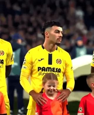 Footballer (Georges Mikautadze) protecting the ears of the mascot girl who seems to be disturbed by the loud stadium sounds