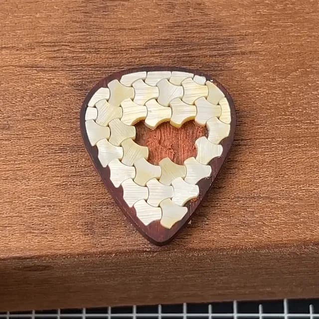 Guitar pick made out of rosewood with geometric shell inlay.