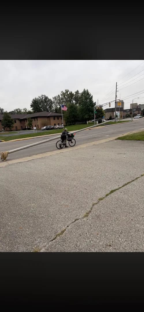 Guy on his bicycle literally has a telephone pole with him dragging it down the street