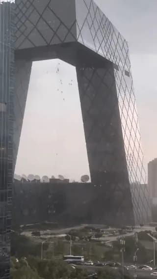 Glass cleaners caught in strong winds dangle from a massive building in Beijing